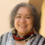 A dark-skinned woman with short, dark curly hair with a red, black, and white scarf and beaded earrings.