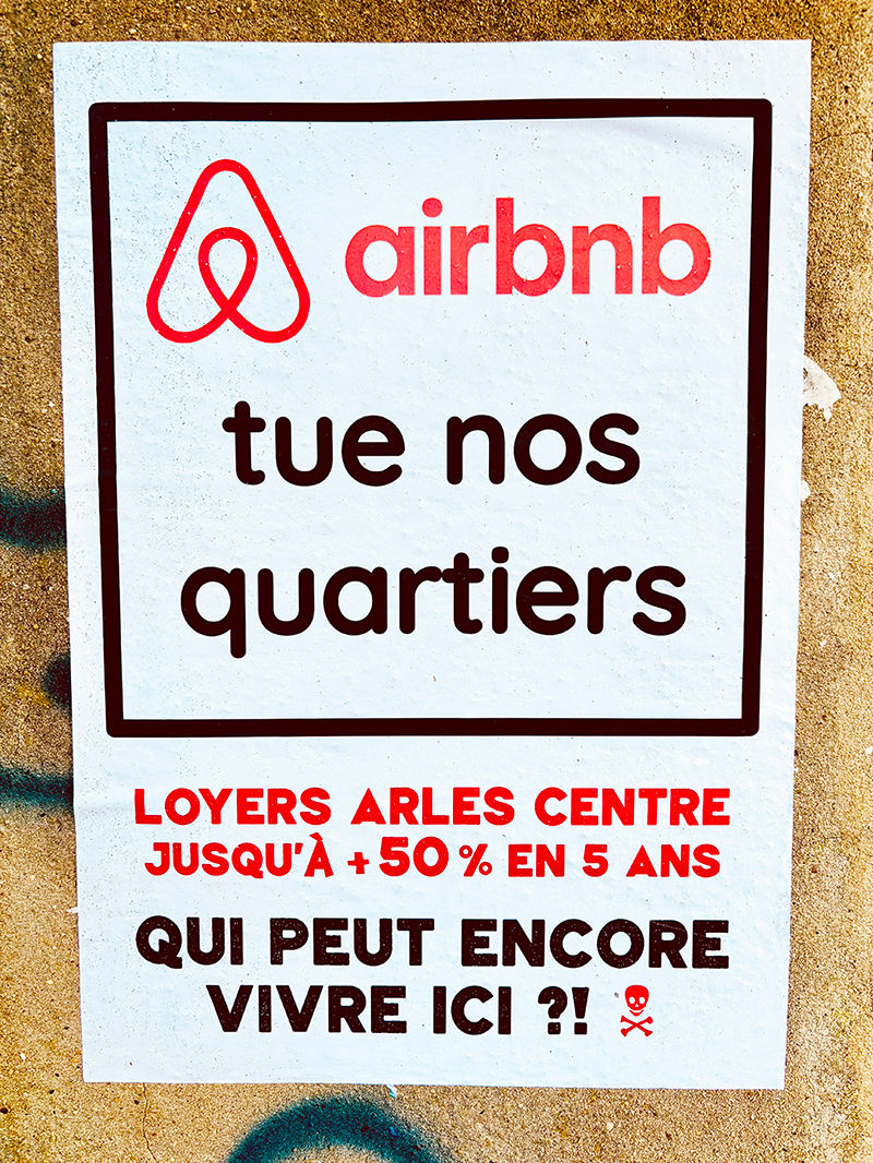 photo représente une affiche sauvage vu dans les rues d'Arles qui dénonce l'impact des location Airbnb sur le marché locatif local avec le message "Airbnb tue nos quartiers - loyers arles centre jusqu'à 50% en 5 ans, qui peut encore vivre ici ?