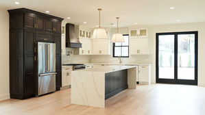 fusion dove and fusion kona cabinets, oak floor, waterfall edge, quartz countertop and backsplash, pot filler, wooden hood, black window and door trim, brass handles, custom kitchen lighting