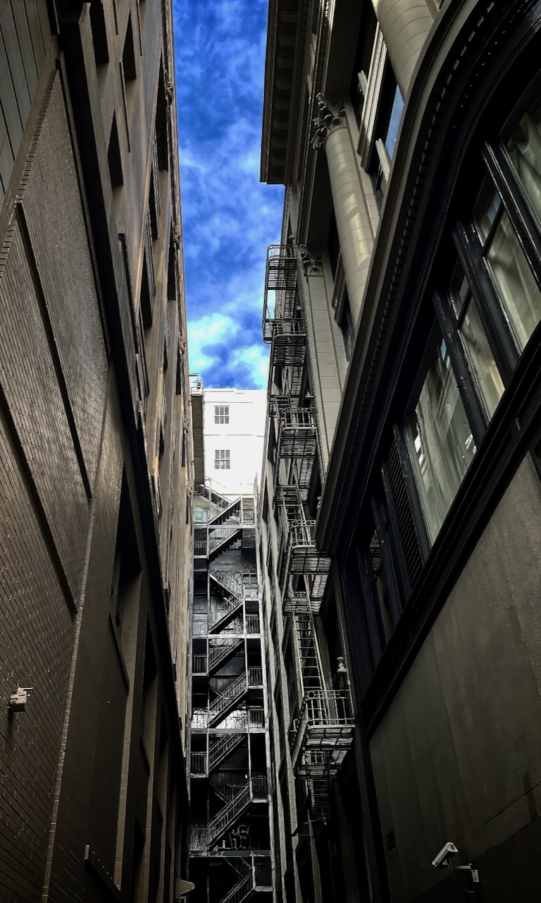 A city alley looking upward between tall buildings.