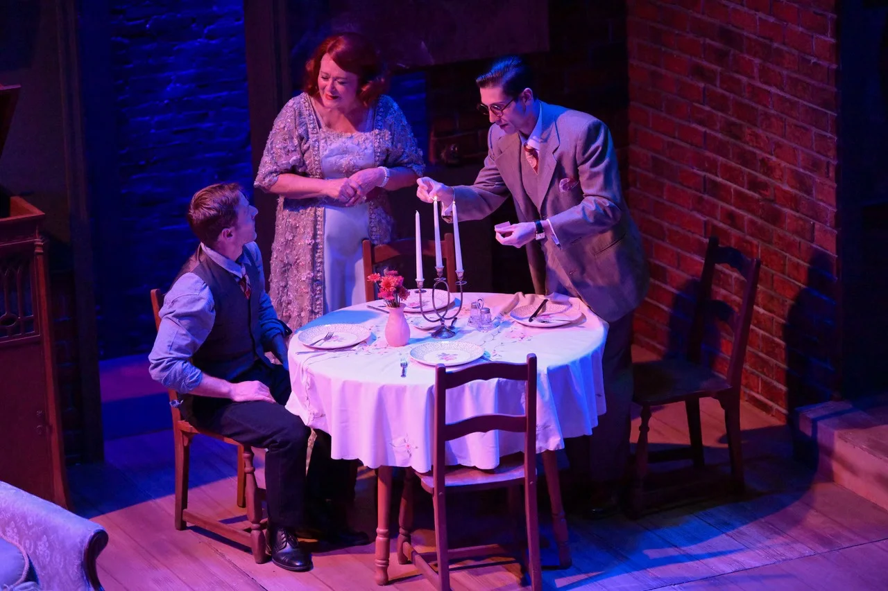 Actors inside the fragile interior world of The Glass Menagerie, framed by the platform, practical furniture, and memory wall.