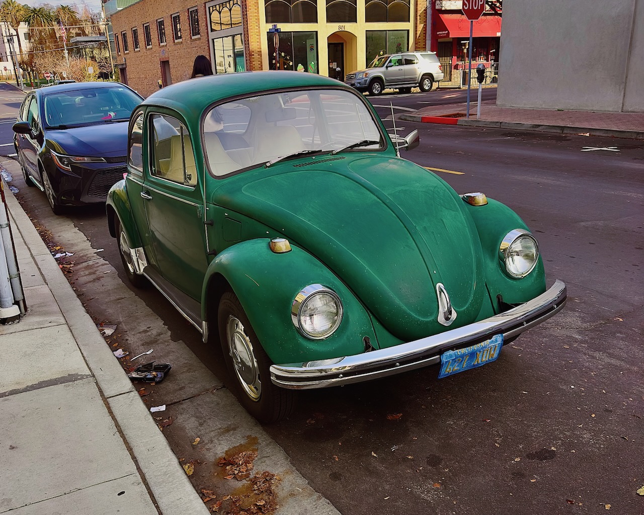A green vintage Volkswagen Beetle parked on a city street.