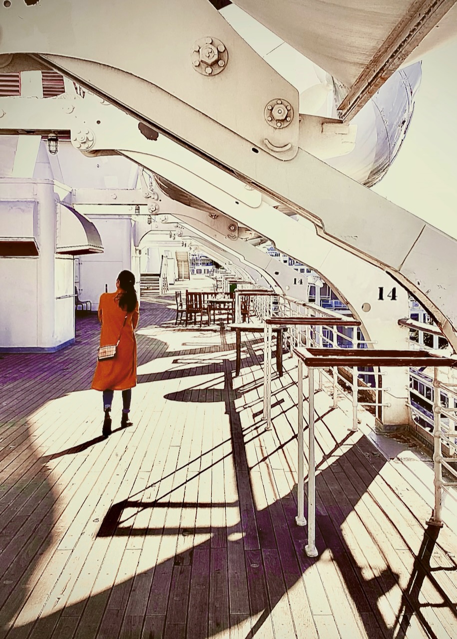 A person walking on a bright ship deck beneath curved davits.