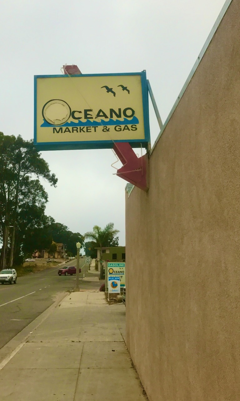 An Oceano Market and Gas sign above a roadside wall.