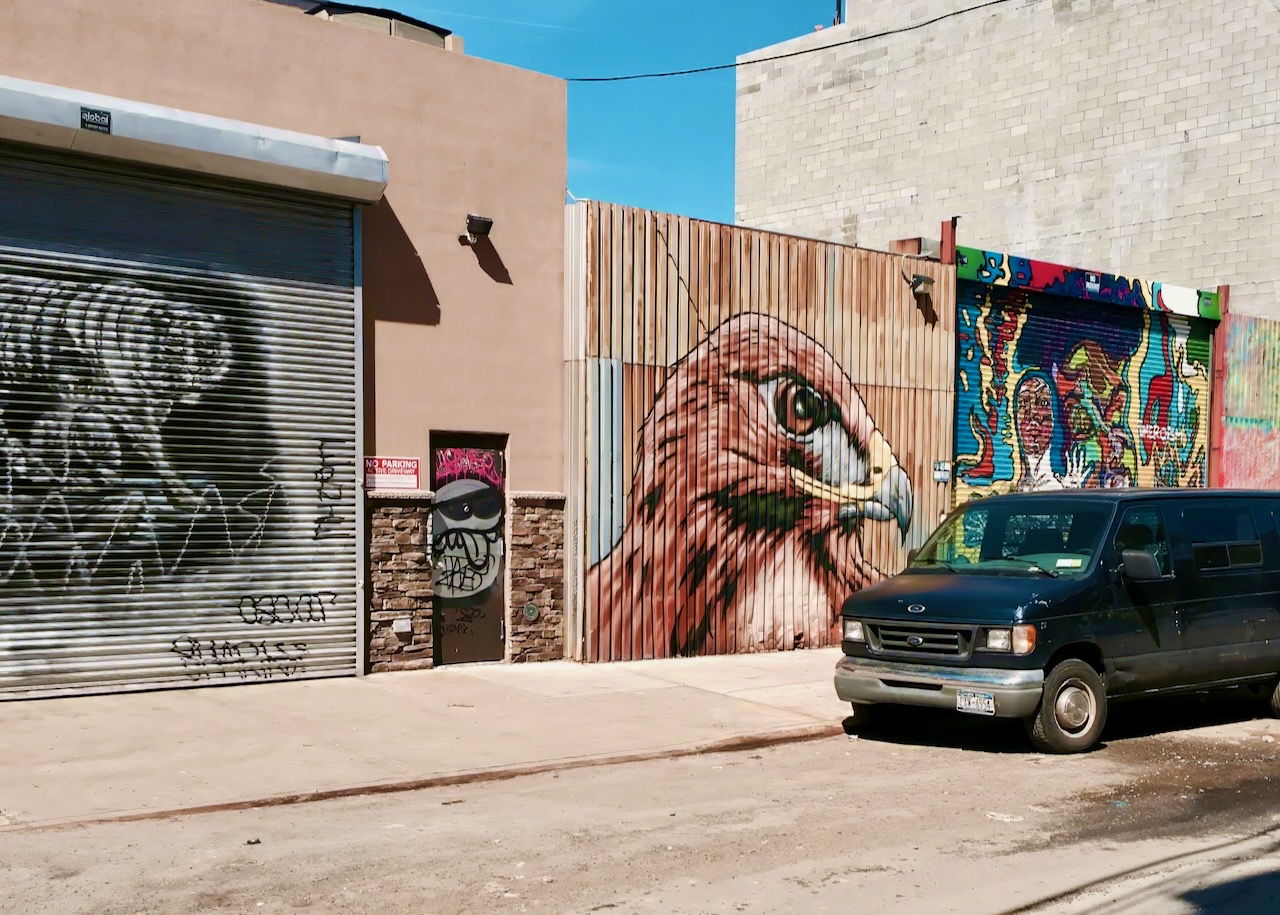 A street with colorful murals on garage doors and a parked van.