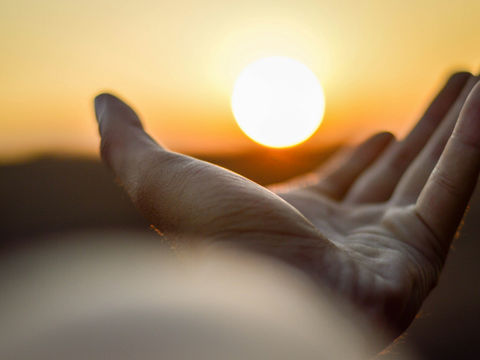 Hand holding the sun at sunrise symbolizing personal growth, new beginnings and inner change