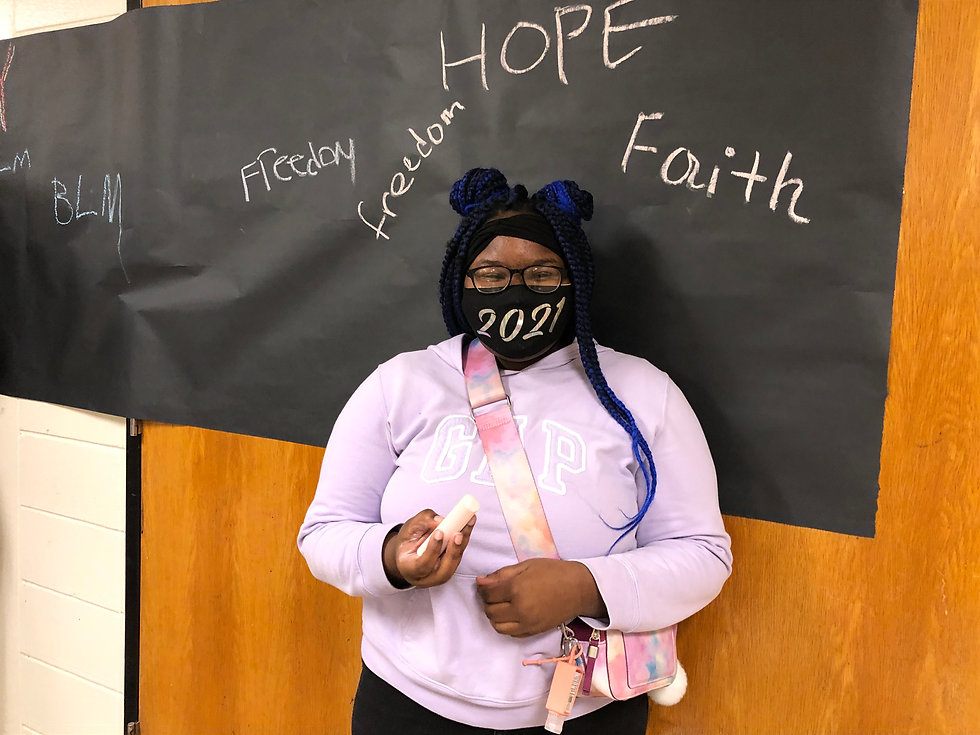 A student in a 2021 face mask stands before a wall with positive words