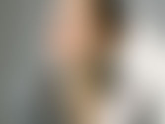 Femme en tailleur gris, assise, regardant vers la lumière. Fond neutre, ton calme et réfléchi, boucles d'oreilles visibles.