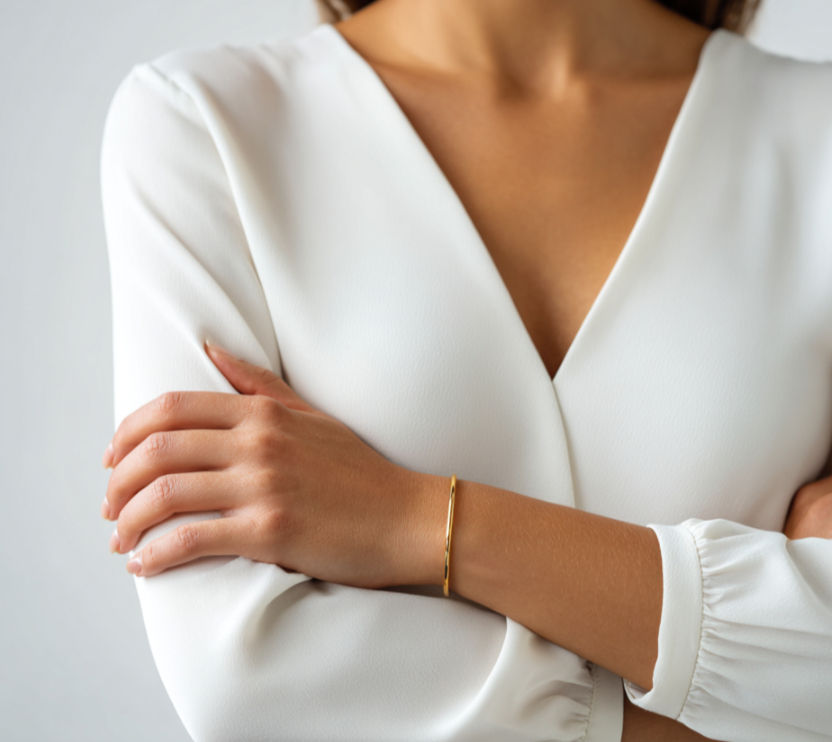 Femme portant un haut blanc, bras croisés avec des manches trop courtes, portant un bracelet doré.