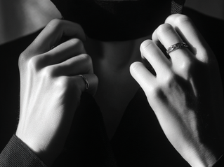 Femme en noir ajustant un col. Deux bagues visibles et une ambiance sophistiquée.