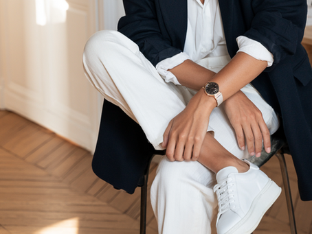 Femme assise, jambes croisées, en blazer marine et tenue blanche, baskets blanches.