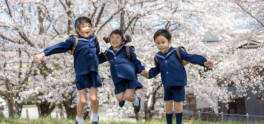 満開の桜の木の前で手を繋いでジャンプする幼稚園生