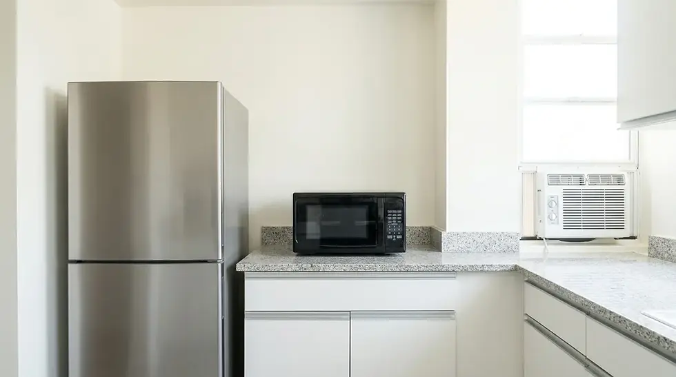 A kitchen scene showing a refrigerator, countertop microwave, and window air conditioning unit — common household appliances typically wired with 12 AWG circuits.