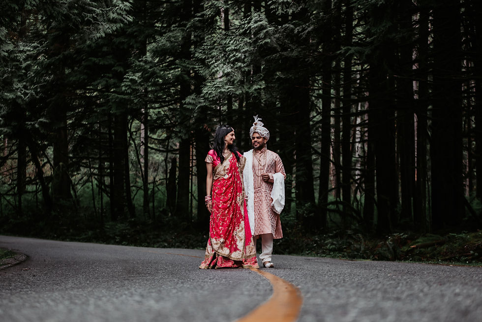 Newly-wed Indian Couple in traditional clothes standing on a curved road in a lush cedar forrest.