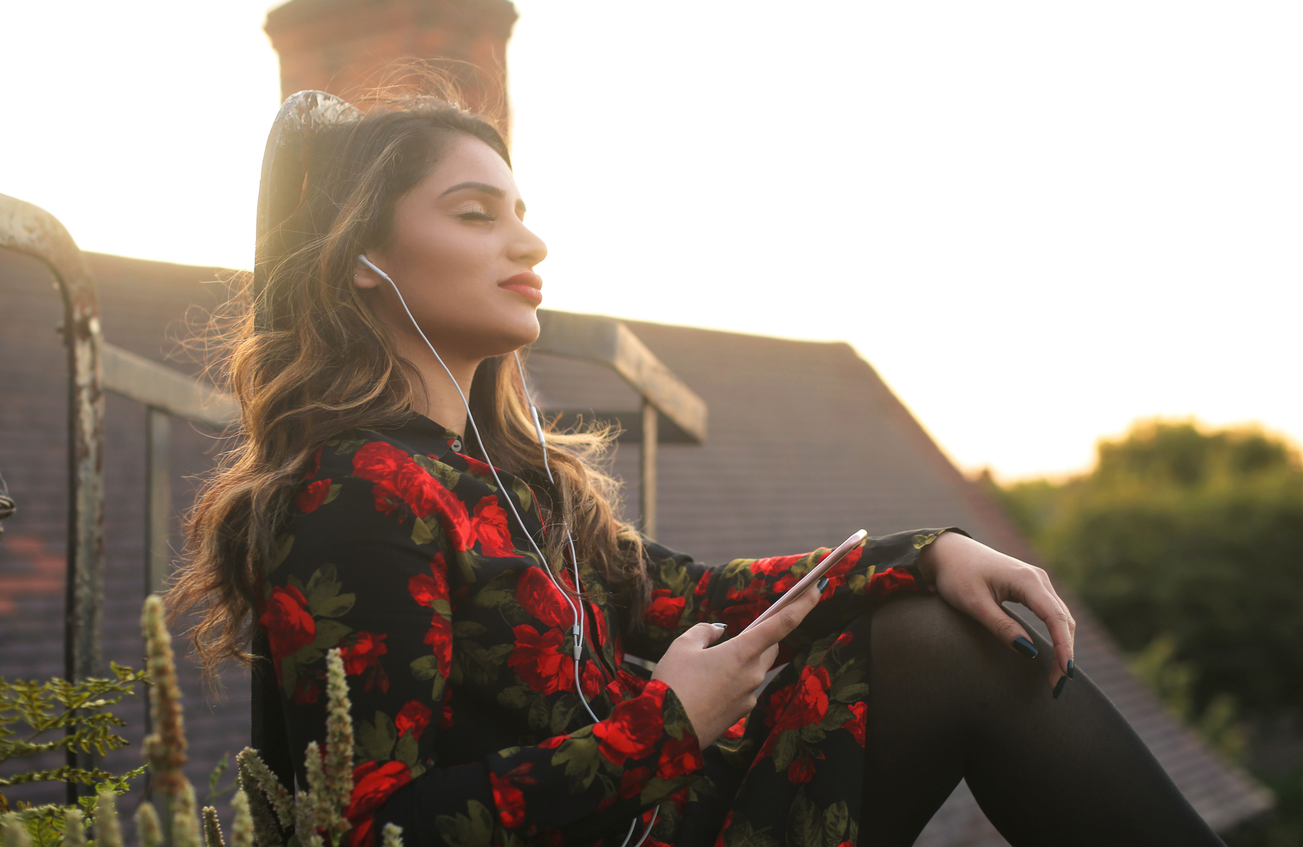 Woman listening to audio from her phone, sitting outside on the grass, with eyes closed in a relaxed attitude