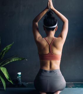 der Rücken einer Yoga Schülerin mit den Händen in der "Namaste" Haltung