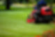 Close up of a red sit on lawnmower cutting a large grass area