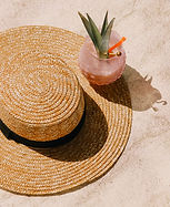 Woven straw hat and pink tropical cocktail on the sand.