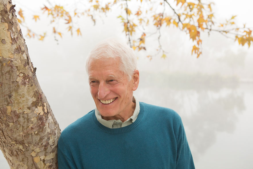 Senior man smiling and leaning against tree