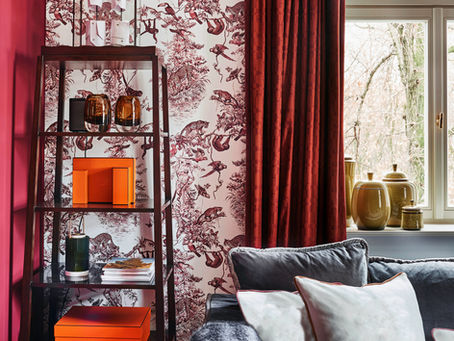 Eclectic Design | Dark red, velvet drapes against a graphic wallpaper with red prints, a cozy, gray, sofa, with statement shelf decors.