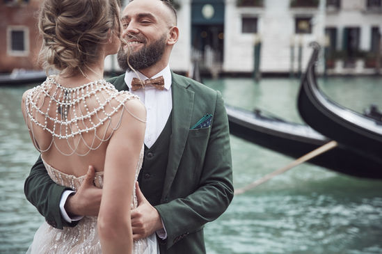 couple about to kiss by a river with a boat and buildings