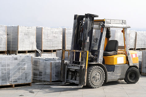 Yellow forklift truck parked in front of plastic wrapped pallets in an outdoor storage yard