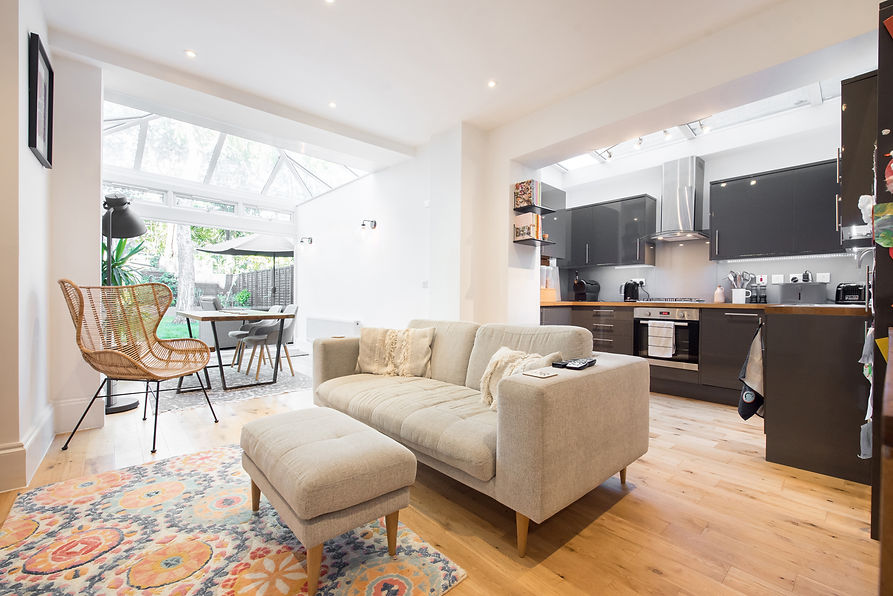 A general interior view of an open plan white painted lounge with sofa, Kitchen with gloss