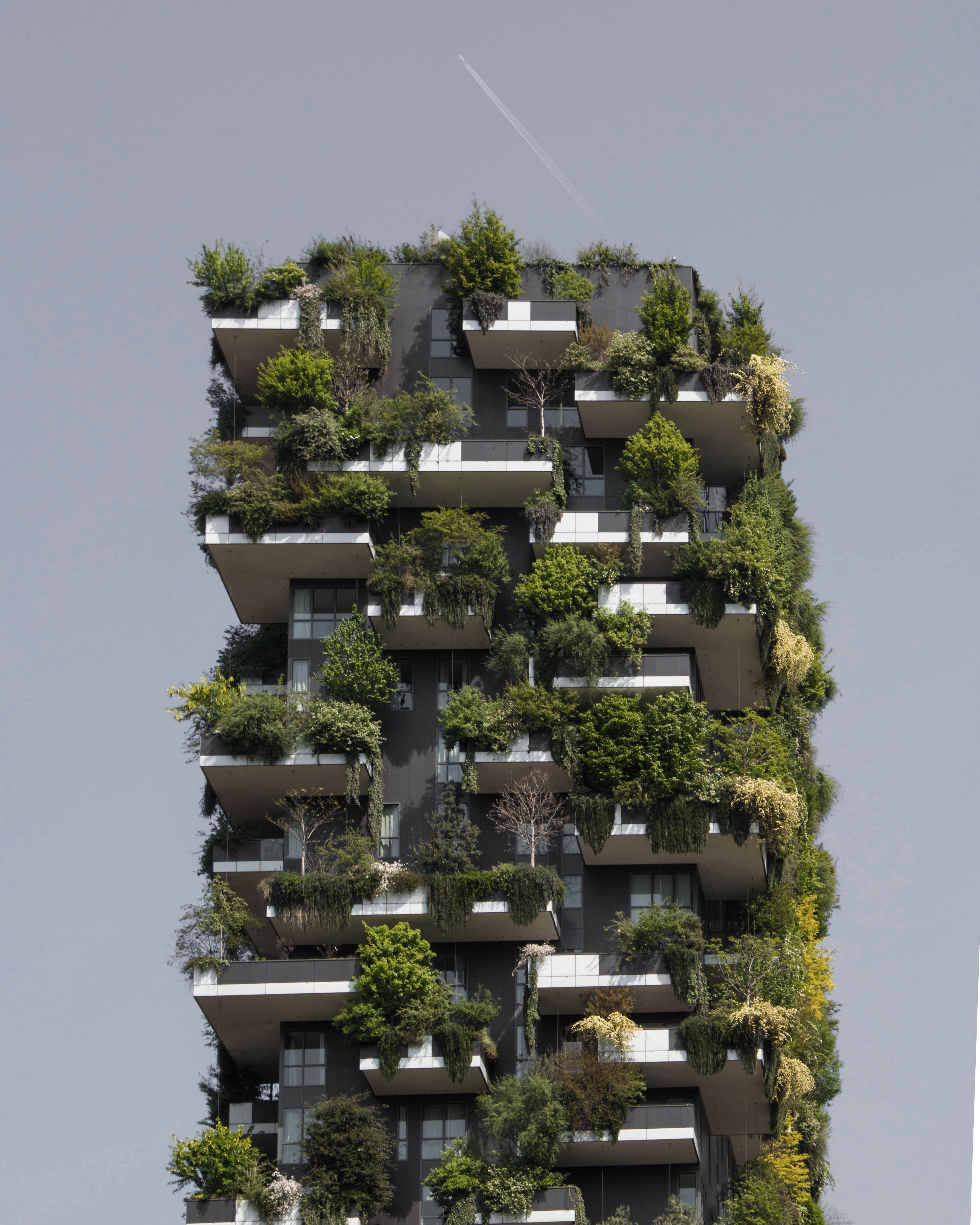 Vertical garden building with greenery on balconies against a clear sky.