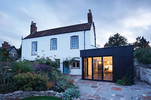 A charming two-story white house with a gabled roof and chimney is complemented by a modern black extension with large windows