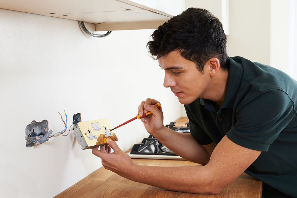 Electrician installing a white electrical socket on a white wall above a wooden countertop in a new house