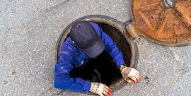 Homem saindo de escotilha de esgoto