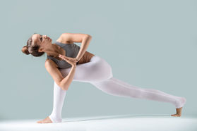 Frau in Yoga-Pose, weiße Hose und graues Top, Yoga-Übung, grauer Hintergrund