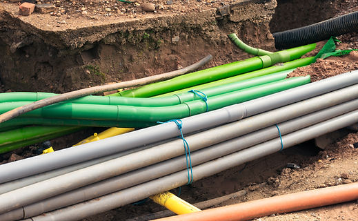 Multiple colored utility pipes laid side-by-side in a ground trench