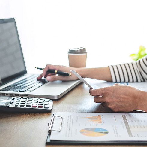 Hands holding paper near a laptop, calculator, coffee cup, and clipboard with graphs