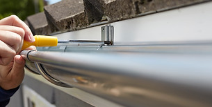 Hand cleaning debris from a white uPVC roof gutter