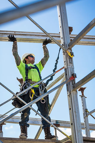 Construction worker in safety gear stands on metal scaffolding, adjusting beams