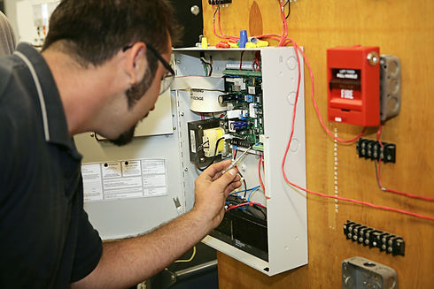Technician using a screwdriver to test wiring in a fire alarm control panel
