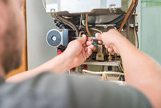 a person using a small screwdriver or voltage tester on the open internal components of a wall-mounted gas boiler or heating system