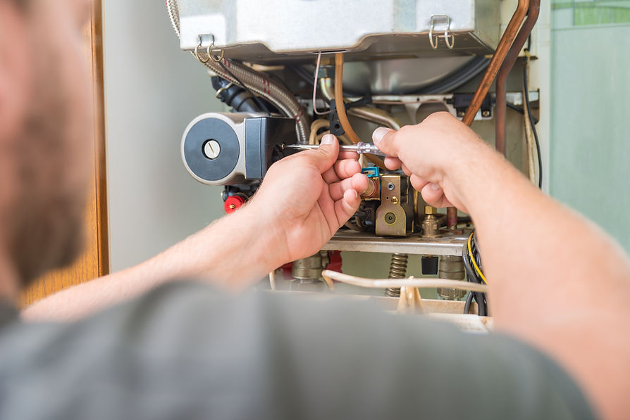 A person repairs a boiler using a wrench, focusing on its intricate parts and wiring