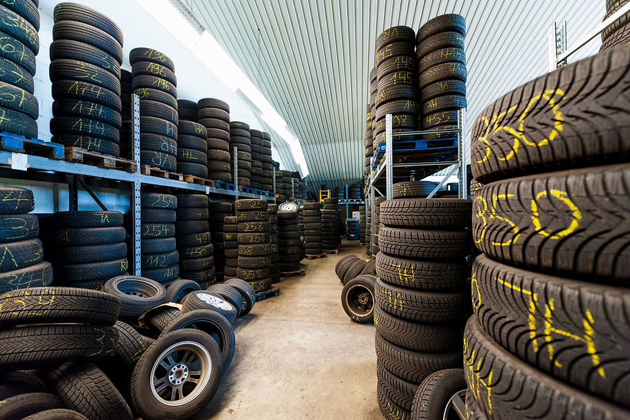Warehouse interior showing high racks and stacks of new and used tyres with yellow markings