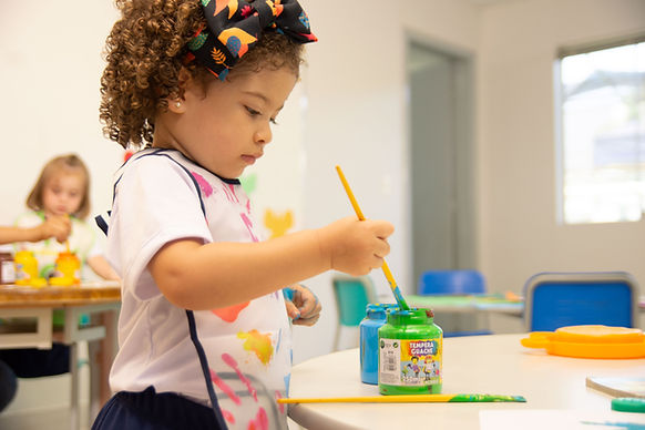 A toddler girl painting in an early childhood classroom.