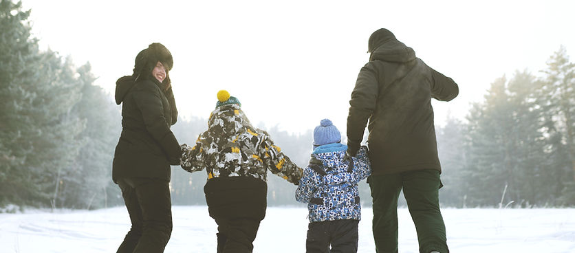 Happy family holding hands while walking together on a snowy path surrounded by trees in winter