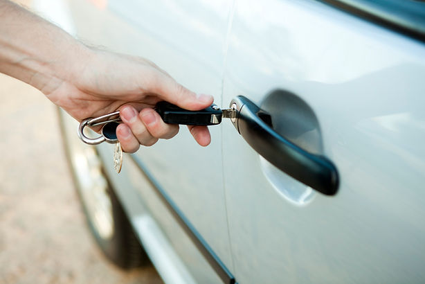Close-up of a hand inserting a key into a silver car door lock