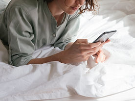 Person laying prone on a bed looking at a cell phone