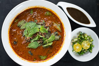 A bowl of rich lamb curry served alongside fresh coriander and sauce