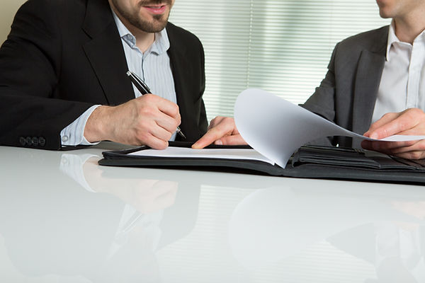 Two hands in formal attire signing documents in a black leather folder