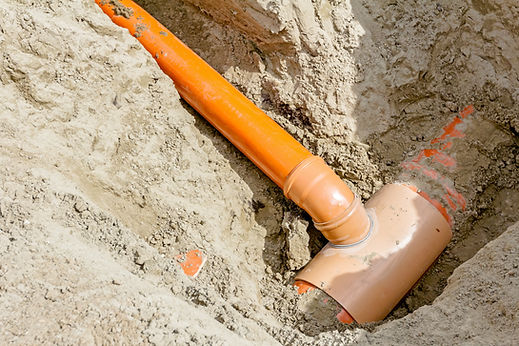 Orange water pipe connected to a junction buried in soil