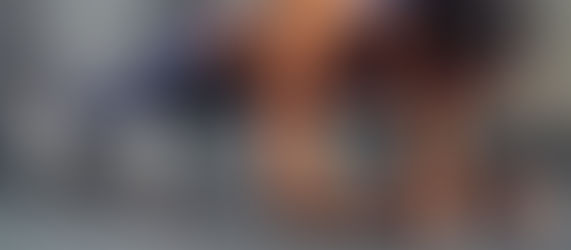 Woman in athletic wear holds a plank position on a concrete floor, focused and determined. Gray walls and braided hair visible.