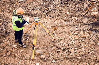 A surveyor in a neon safety vest and hard hat stands on rocky terrain