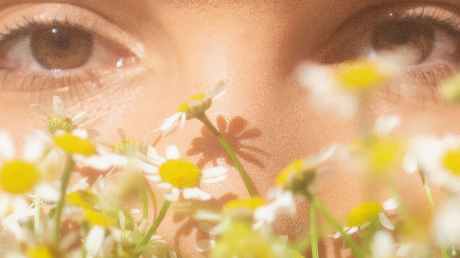 A woman looks through flowers into the camera.